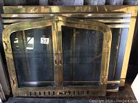 Close-up photo of arch brass fireplace screen with glass doors showing the polished brass frame and glass panels.
