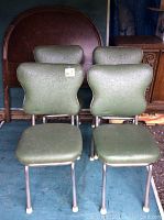 Close-up of two vintage green vinyl and chrome chairs showing backrest shape and seat detail