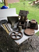 Overview of all items on table, showing wooden birdhouse, office trays, stone grinder, pulley wheel, wall column and various metal parts