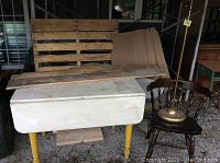 Photo of the farmers drop leaf table, tavern chair, wooden plate shelf, and brass floor lamp showing overall lot contents from an angle.