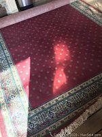 Photo of the wine red wool rug with small repeating motifs and detailed multicolor border with fringe on floor.