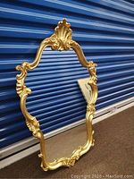 Full view of gold ornate wall mirror leaning against blue storage door