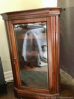 Front view of mahogany wine rack with closed glass door, brass knob, and decorative crown molding top.