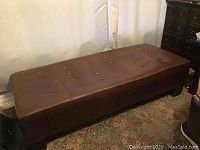 Angled view of the brown leather tufted bench showing top and legs
