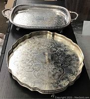 Photo showing the two silver plated trays: rectangular tray with handles and round ornate Primrose tray with scalloped edge and intricate engraving.