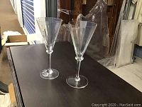 Two crystal stemmed glasses with 12-sided design on a dark surface, showing shape and clarity.