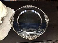 Single silver-plated round plate charger with intricate embossed detailing on rim, visible surface scratches.