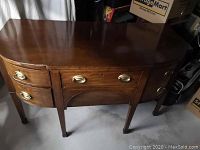 Sideboard front view showing curved drawer fronts, brass handles, and wood surface with scratches and slight wear.