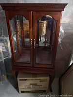 Front view of curio cabinet on its stand showing dual glass doors, crown molding and metal handles