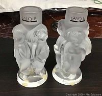 Front view of both candlesticks showing frosted cherub relief and Lalique Paris labels on holders