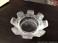 Glass candy dish with multiple sculpted faces around the edge on a dark surface.