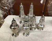 Photo of three pairs of silver salt and pepper shakers of varying sizes on white cloth