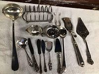 Photo showing a collection of 14 silver serving pieces including ladle, toast holder, small bowls, condiment spoons, spreaders, and serving utensils.