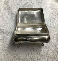 Small silver-plated pill box with hinged lid opened to show interior