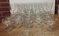 Front view of 23 pieces of clear glass stemware with etched floral and swirl designs, arranged in three rows showing variety of glass shapes and sizes.
