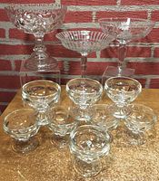 3 glass compotes with distinct patterns and 8 Federal sherbet glasses arranged on a table against brick background