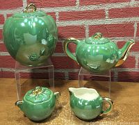 Photo of entire set showing cookie jar, teapot, creamer, and sugar bowl on wooden surface against brick wall