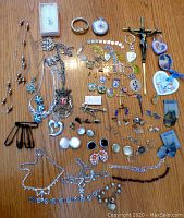 Full view of all jewelry items displayed on a wooden surface including necklaces, earrings, religious items, pins, and chains.