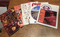 Five vintage Phillies baseball publications laid out flat on a table, including World Series and yearbooks.