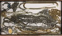 Top view of display case with an assortment of silver and gold toned necklaces and chains tangled together, including decorative pendants.