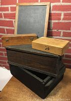 Overview photo of all items stacked including the slate leaning on wall, two smaller wooden boxes on top, and larger dark and black boxes below.