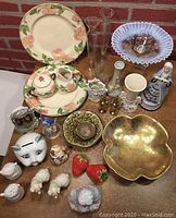 Photo showing miscellaneous ceramic and glass collectibles including floral patterned plates and creamers, glass vases, gold-colored bowl, and figurines.