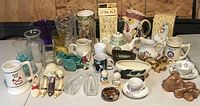 Full view of mixed collectibles and glassware, showing ceramic pitchers, mugs, figurines, and glassware