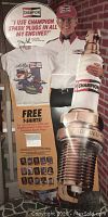 Front view of the large cardboard stand-up advertising display featuring Joe Gibbs holding a large Champion Spark Plug and promotional messaging about free T-shirts.