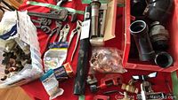 Various plumbing tools and fittings including pipe cutters, pipe wrench, brass connectors and plastic pipes on red cloth.