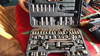 Open socket wrench set showing various sized sockets, ratchet handle, and attachments with visible surface rust and corrosion on tool bits in a black plastic case on a table.