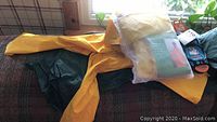 Photo showing yellow and green waterproof ponchos and rain coats laid on a fabric surface, some items inside mesh bags
