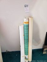 Three rolled posters/maps standing against wall, one identifiable as 'Neils'