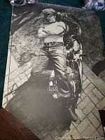 Black and white poster of a man laying on motorcycle sideways with folded arms and license plate visible (63 632).