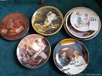 Collector plates with colorful artwork and decorative borders including maritime, children, and family scenes arranged on carpet