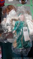 Three porcelain dolls wrapped in plastic bags displayed together, showing detailed costumes and hair styles.