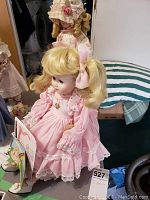 Front view of two porcelain dolls including Knowles Meagan in pink dress holding COA and papers.