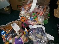 Three large clear bags filled with assorted Beanie Babies, plush toys, and dolls placed on carpet, showing variety and quantity.
