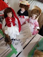 Three Danbury Mint collectible dolls displayed together on a bed, showing details of their outfits and COAs beneath them