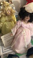 Photo showing Cinderella doll in yellow dress with curled blonde hair holding a paper (likely COA)