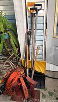 Wide view of yard tools including snow shovel, rake, pry bar, hatchet, long handled tools, orange extension cords, and red lantern.