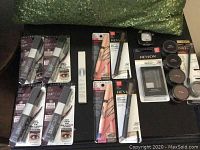 Four Maybelline Snapscara Mascaras, brow sets from Revlon and L'Oreal, mousse sticks, brow definers and compact makeup items laid out on black surface with green pillow background