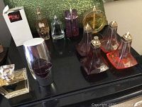 Overview photo showing eleven assorted bottles of perfumes including clear, purple, amber and orange colors with packaging box for Tabu.