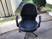Front view of the black padded office chair showing seat, backrest, armrests, and wheels.