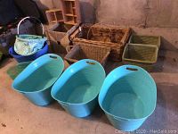 Three large matching turquoise blue plastic tubs with cutout handles and several wicker baskets behind them.