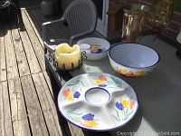 Three-piece hand painted glazed ceramic set with floral tulip patterns alongside amber colored glass vases and metal candle holder on outdoor table