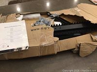 Open box showing black metal frame parts and mounting hardware inside cardboard packaging.