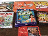 Top view of the 7 board games showing box art for Clue Carnival, Green Eggs and Ham, Upwords, Monopoly Junior, Hullabaloo, Pin The Tail On The Donkey, and Stand Back Exploding Science Lab