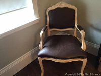 Front view of the chair showing leather seat and backrest with nailhead trim and carved wood frame.