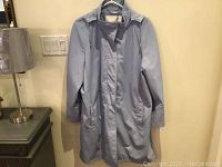 Full view of light blue jacket hanging on white hanger with a lamp and light switch visible nearby.