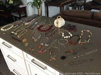 Wide view of various costume jewellery necklaces laid out on a dark surface, showing a variety of bead types, chains, and pendants.